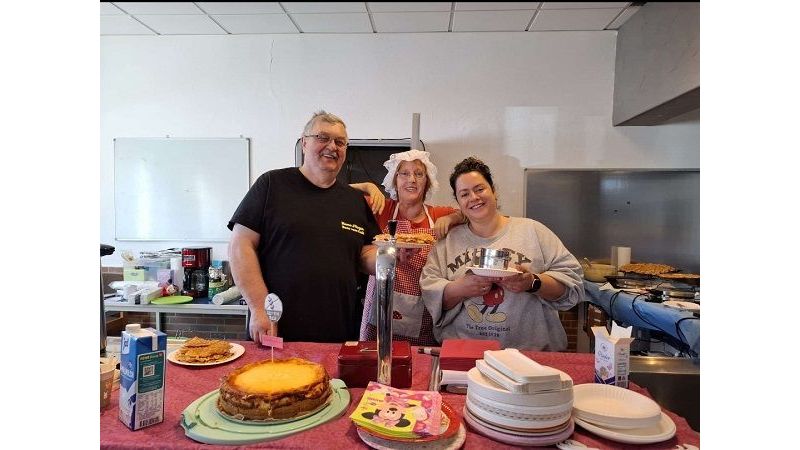Drei Personen stehen hinter dem Kuchenstand und halten Waffeln in die Kamera