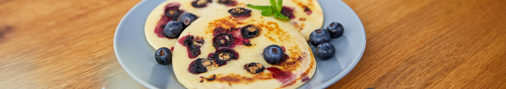 Das Bild zeigt die fertigen Pfannkuchen mit Blaubeeren und einem Minzblatt verziert.