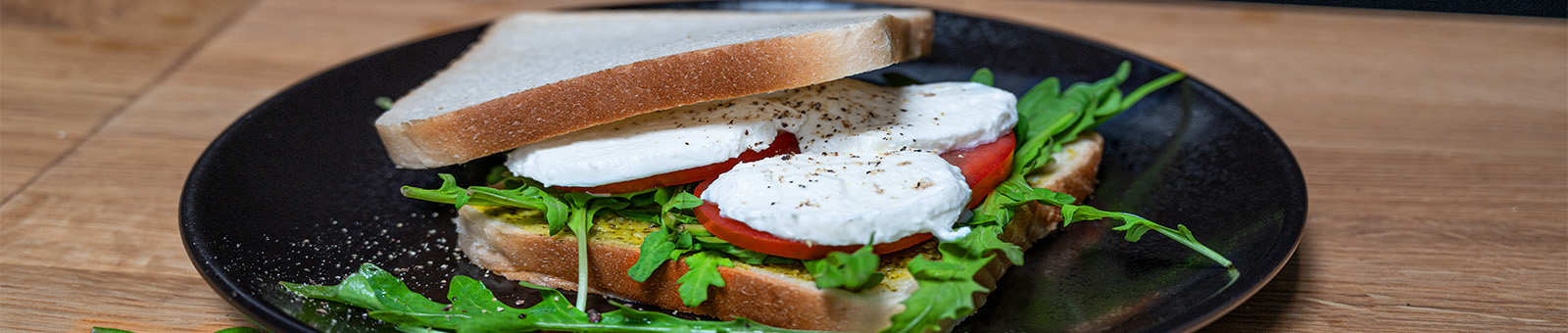 Das Bild zeigt ein Sandwich belegt mit Tomaten, Rucola und Mozzarella.