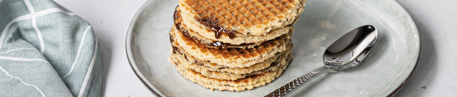 Das Bild zeigt Stroopwaffeln mit Sirup auf einem grauen Teller.