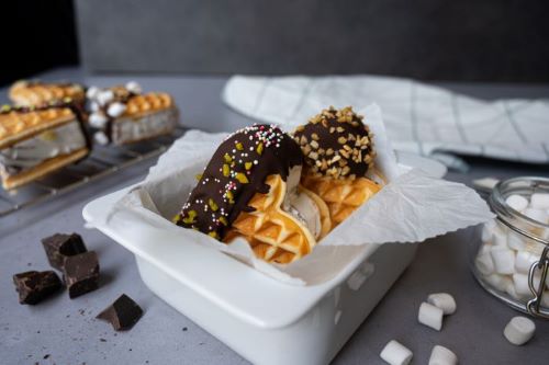 Das Bild zeigt zwei Eiswaffelsandwiches mit Schokolade, Mandelblättchen und gehackten Nüssen verziert.