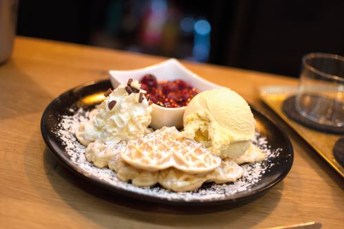 Das Bild zeigt einen Teller mit Waffeln, Vanilleeis, Sahne und heißen Kirschen. 