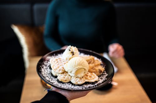 Das Bild zeigt eine Waffel mit Bratapfelkompott, Vanilleis und Schlagsahne. 